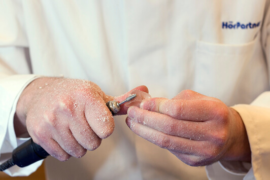 Ein Hörakustiker bearbeitet ein Hörgerät handwerklich mit einem speziellen Werkzeug.